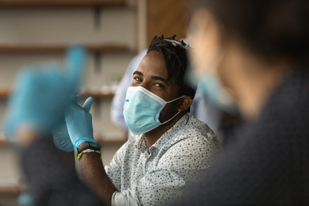 Crop close up of smiling African American man in facial mask and rubber gloves talk with colleagues at workplace. Biracial male worker in facemask speak with coworker during corona covid-19 pandemics.の写真素材