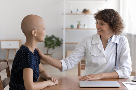 Happy female cancer patient tell she is feeling better to trusted doctor on appointment at hospital. Pleasant woman therapist hold hand on shoulder of sick young lady share good news about her healthの写真素材