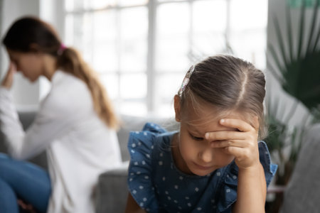 Close up upset little girl and mother ignoring each other after quarrel, sitting back to back on couch at home, frustrated daughter and worried mum avoiding talk, parent and child conflict conceptの写真素材