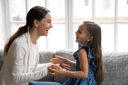 Close up overjoyed mother and little daughter playing patty cake, sitting on couch together, happy young mum and adorable girl child having fun, spending leisure time at home, involved in active gameの写真素材