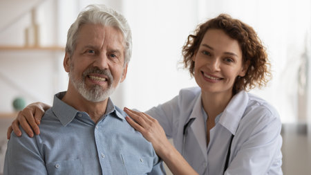 Portrait of smiling kind young female general practitioner or nurse embracing shoulders of happy elderly senior retired man. Friendly physician and middle aged pleasant male patient looking at camera.の写真素材