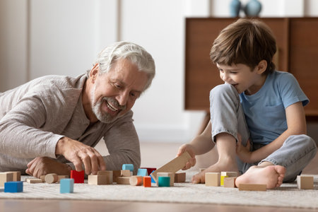 Loving elderly Caucasian grandfather have fun playing with little 6s boy child building with blocks. Happy caring mature grandparent engaged in funny game activity with small grandson at home.の写真素材