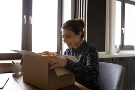 Excited young Indian woman unpack cardboard box shopping online feel overjoyed about good package....