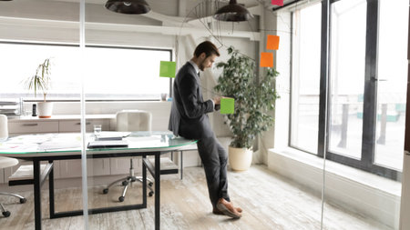 Wide banner over glass wall view of businessman stand in own office use modern tablet gadget for business purpose. Male CEO or director look at pad device screen consult client or browse internet.の写真素材
