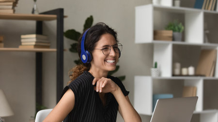 Overjoyed millennial Caucasian woman in headphones and glasses talk speak on video call on laptop. Smiling young female in earphones have fun working on computer have online meeting at home office.の写真素材