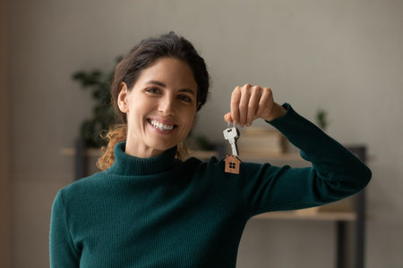 Portrait of smiling young Caucasian woman hold keys to new home relocate to own apartment or dwelling. Excited millennial female renter or tenant celebrate moving to house. Rental, estate concept.の写真素材