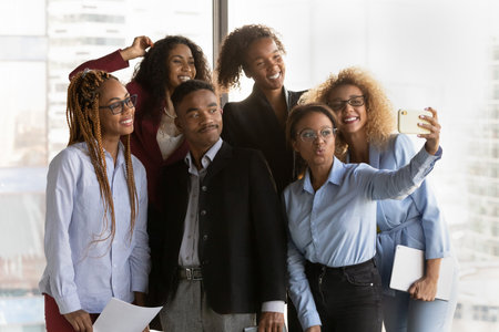 Happy diverse multiethnic colleagues have fun make self-portrait picture on cellphone together. Smiling young multiracial businesspeople pose for selfie on smartphone in office. Technology concept.の写真素材