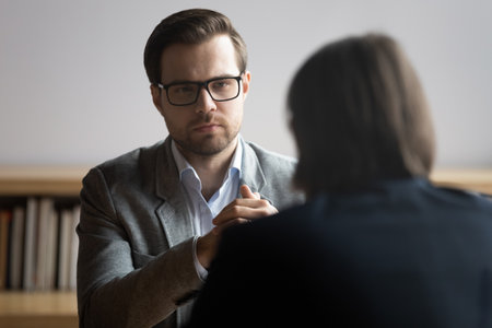 Concentrated male hr manager in glasses listening to job candidate, involved in conversation during interview in office. Skilled 30s financial advisor giving professional consultation to client.の写真素材