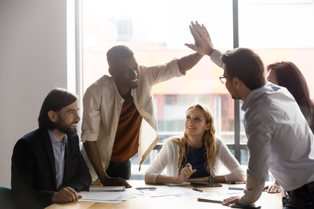 Happy young african american employee giving high five to smiling 30s male team leader at colleagues group brainstorming meeting, celebrating successful project finish or sharing corporate success.の写真素材