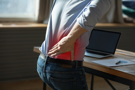 Close up rear view stressed young man touching lower back feeling discomfort, suffering from sudden...