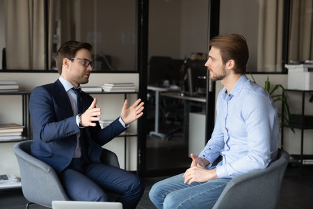 Confident businessmen discussing project or deal, business partners negotiations or job interview in modern office, colleagues talking, sharing ideas, working together, manager consulting clientの写真素材