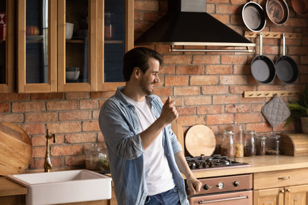 Happy millennial Caucasian man dance in own modern renovated kitchen on lazy leisure weekend at home. Overjoyed young male renter or tenant celebrate relocation to new house. Rental concept.の写真素材