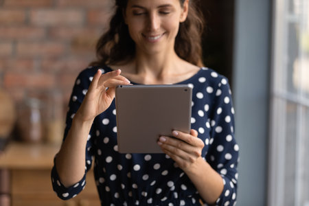 Close up of smiling young Caucasian woman hold use table gadget communicate online. Happy millennial female client or user look at pad screen browse wireless internet on device. Technology concept.の写真素材