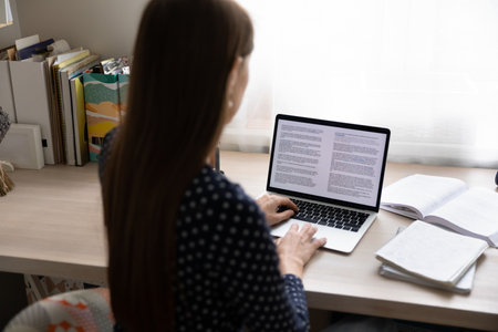 Paperwork on computer. Back view of young lady working from home focused on pc screen read...
