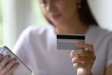 Paying online is easy. Close up of young lady holding credit card providing cashless transaction using online e-banking technology. Millennial woman checking bank account status via mobile phone appの写真素材