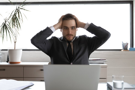 Close up shocked businessman touching head, looking at laptop screen with wide open eyes, amazed executive manager wearing suit reading unexpected bad news in email, bankruptcy, financial problemの写真素材
