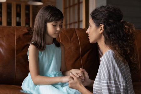 Close up caring young mother comforting calming upset offended little daughter, holding hands, sitting on couch, mum expressing love and support, child psychologist concept, psychological helpの写真素材