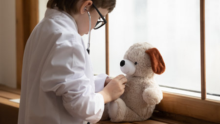 Caring small boy child in white medical uniform hold stethoscope play hospital game examine fluffy toy bear. Little 7s kid act as doctor cure stuffed animal dream of future medicine clinic career.の写真素材
