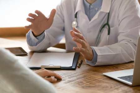 Close up of male doctor in white medical uniform sit at table in hospital talk consult female...