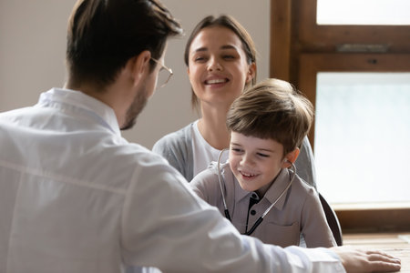 Happy small 7s boy patient have fun play with caring male pediatrician at consultation with mom in hospital. Smiling little child engaged in funny game with playful man doctor at visit to clinic.の写真素材