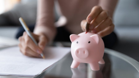 Close up young woman putting coin in piggy bank, writing household expenses on paper, planning...