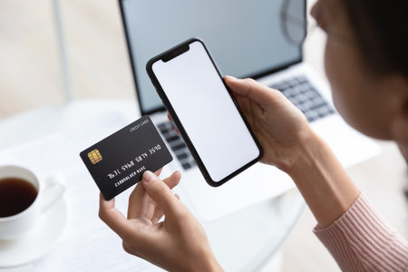 Close up young woman holding bank credit card and modern tech device with mock up white screen in hands, enjoying purchasing goods in internet store using mobile phone application, online shopping.の写真素材
