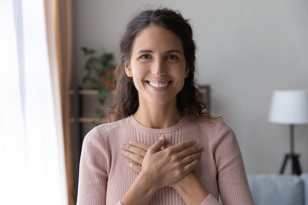 Portrait of happy millennial female volunteer holding folded hands on chest, looking at camera. Kind smiling young woman feeling thankful, showing appreciation, gratitude believe charity concept.の写真素材