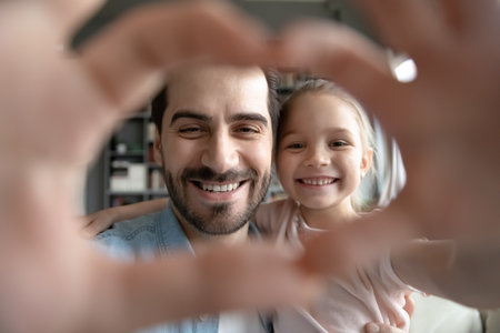 Head shot close up happy young caucasian father and playful cute small child daughter making heart symbol with fingers, enjoying spending free time together at home, loving family relations concept.の写真素材