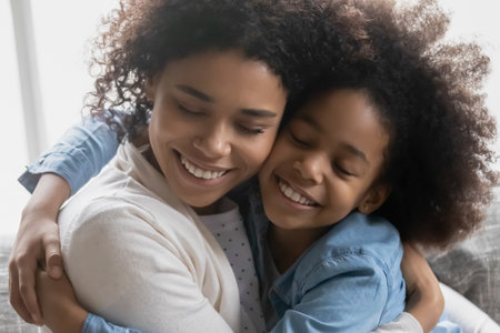 Close up head shot happy African American mother and little daughter hugging, touching cheeks, family enjoying tender moment, young mum and adorable girl child cuddling, expressing support and loveの写真素材