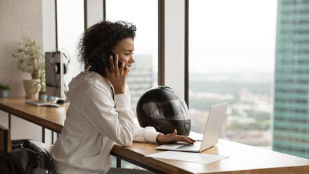 Busy african woman enjoying biker style consult client by phone place order on website using laptop...