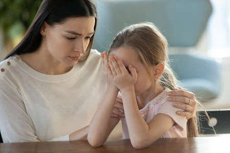 Loving young Caucasian mother hug comfort upset sad small 7s daughter crying at home. Caring mom...