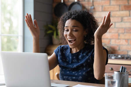 Close up overjoyed African American woman looking at laptop screen, excited by good news, reading email, online lottery win or money refund, job promotion, student received great exam resultsの写真素材