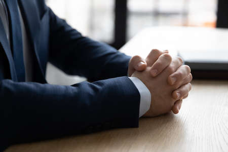 Close up of successful businessman in suit sit at desk in office hold hands clasped clenched thinking pondering. Confident male CEO or director in formalwear make plans or decide. Leadership concept.の写真素材