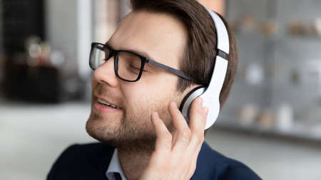 Close up of calm happy young Caucasian businessman wear headphones enjoy good quality sound on...