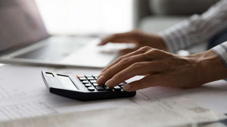 Close up cropped view of young woman accountant auditor doing paperwork at desk full of financial...
