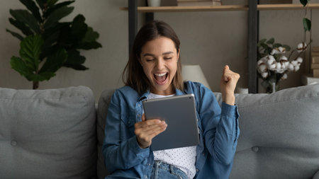 Emotional young female sport fan scream yes watch winning victory of favorite team on pad pc online. Excited woman student read email from college about getting scholarship for personal achievementの写真素材