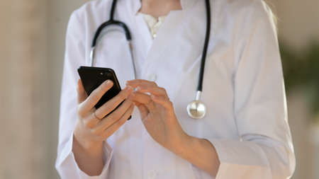 Close up young female doctor using modern tech mobile gadget, web surfing information, improving...