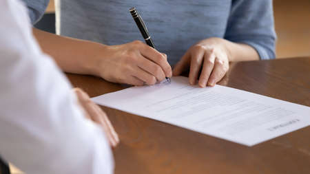 Close up young woman signing medical insurance service contract with chosen family doctor at...