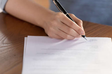 Close up focus on female hand putting signature at paper contract document. Young woman signing...