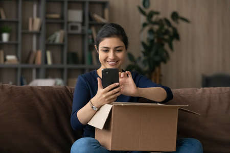 Smiling millennial Indian woman rate or track parcel order on cellphone shopping online on gadget...