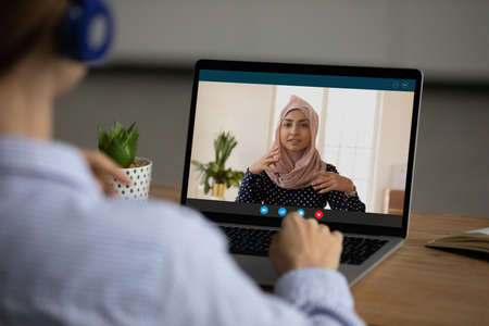 Over shoulder of female employee talk speak on video call with muslim business partner or client....