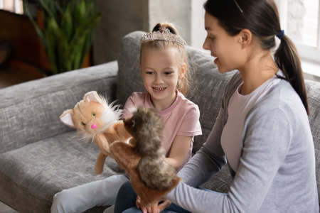 Happy mum and excited daughter girl wearing princess tiara talk play toy fluffy hand puppets...