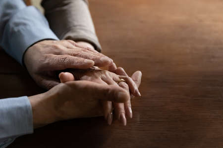 Senior mature man holding hand of beloved middle aged wife. Old family couple enjoys time together, expressing love, affection and support. Close up of arms with wedding ring. OAP Relationship conceptの写真素材