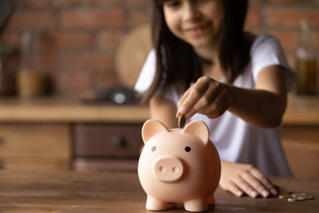 Crop close up of provident economical small girl kid put money into piggybank saving for future needs. Happy smart little 9s teen child make donation contribution in piggy bank. Investment concept.の写真素材