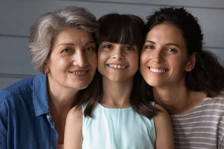 Close up portrait of happy three generations of Hispanic women, child, mom and grandma, pose together. Smiling Latino little girl kid with mother and grandmother show family unity and bonding.の写真素材