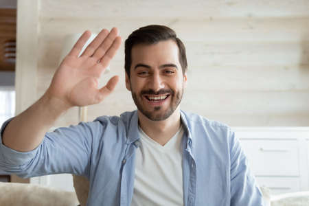 Smiling millennial Caucasian man wave look at camera having video call using unlimited wireless internet connection at home, happy young male greeting talk speak on webcam, technology conceptの写真素材