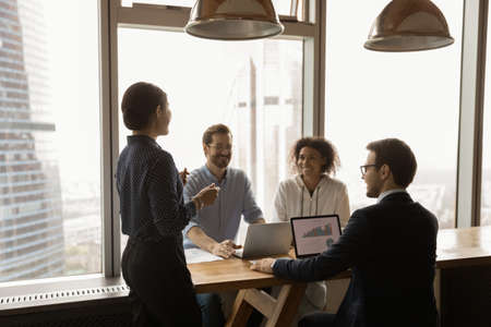Indian businesswoman mentor leading corporate meeting in modern office with panoramic windows, boardroom, smiling colleagues sharing ideas, business partners discussing project strategy, negotiatingの写真素材