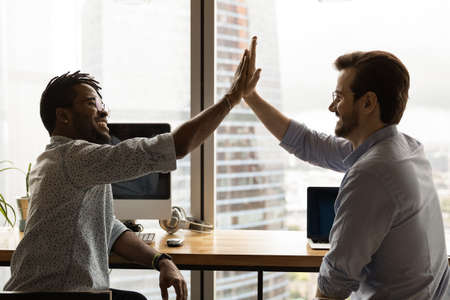 Side view overjoyed diverse colleagues giving high five, celebrating success, African American and...