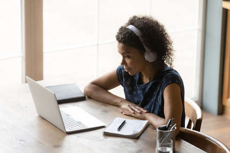 Thoughtful millennial african woman student in headset listen to teacher ponder on video information...