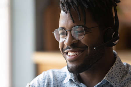 Close up of young smiling afro american guy wearing headset technical support worker dispatcher. Friendly black man call center operator in wireless headphones contact client glad to help. Copy spaceの写真素材